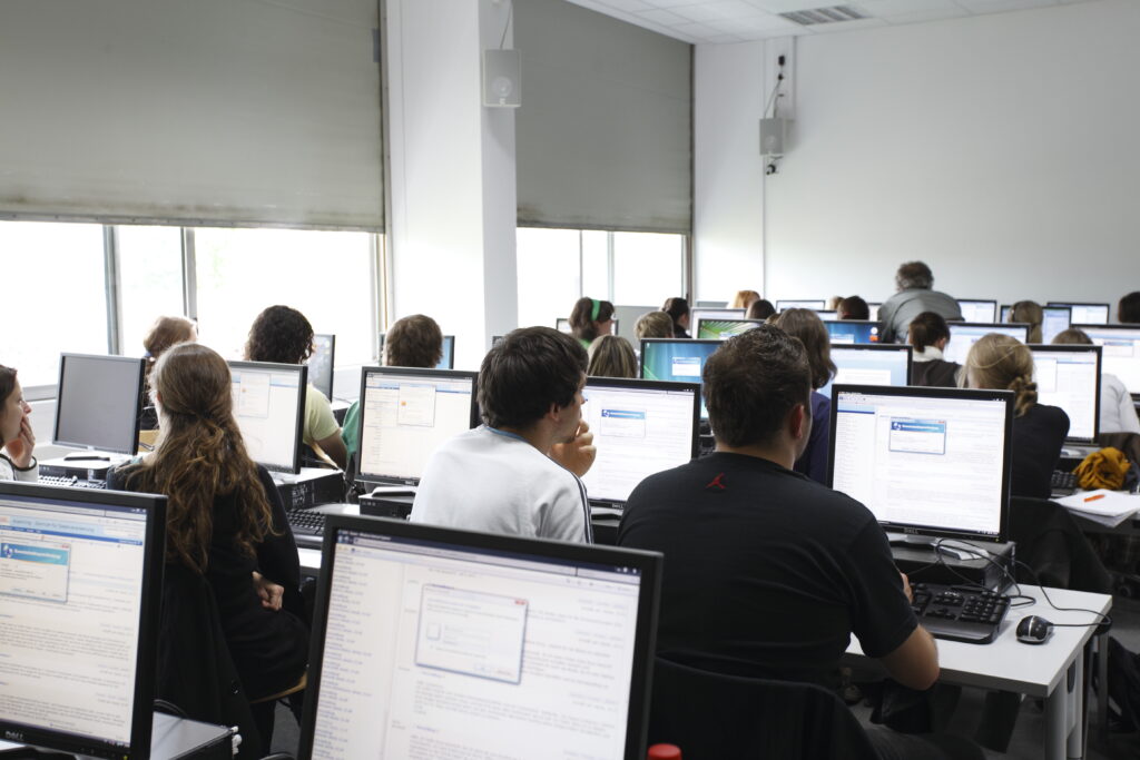 PC-Pool Raum. Arbeitsplätze sind mit PC, Bildschirm, Tastatur und Maus ausgestattet. Die Tische sind in Reihen aufgestellt mit jeweils 5 Arbeitsplätzen pro Reihe.